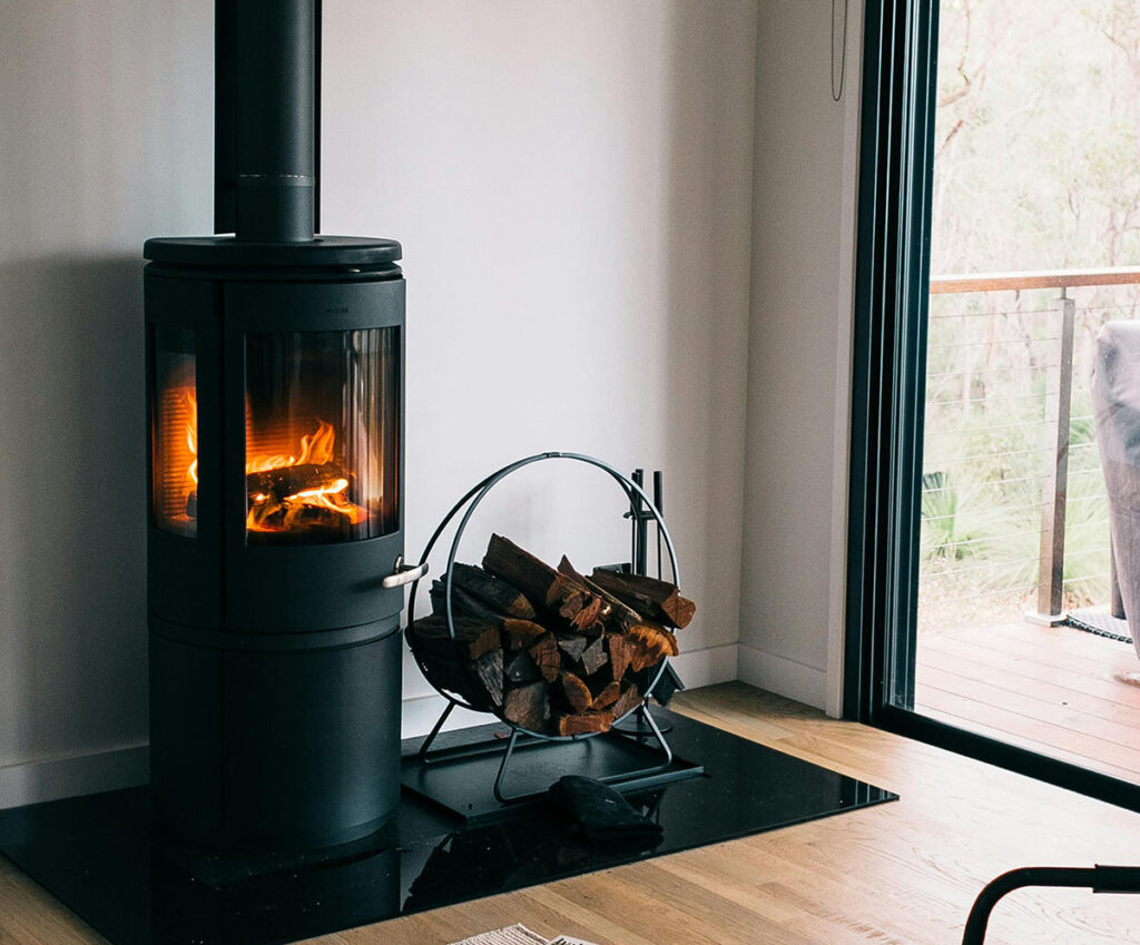 Wood burning in a modern wood stove next to a firewood rack and a sliding glass door.